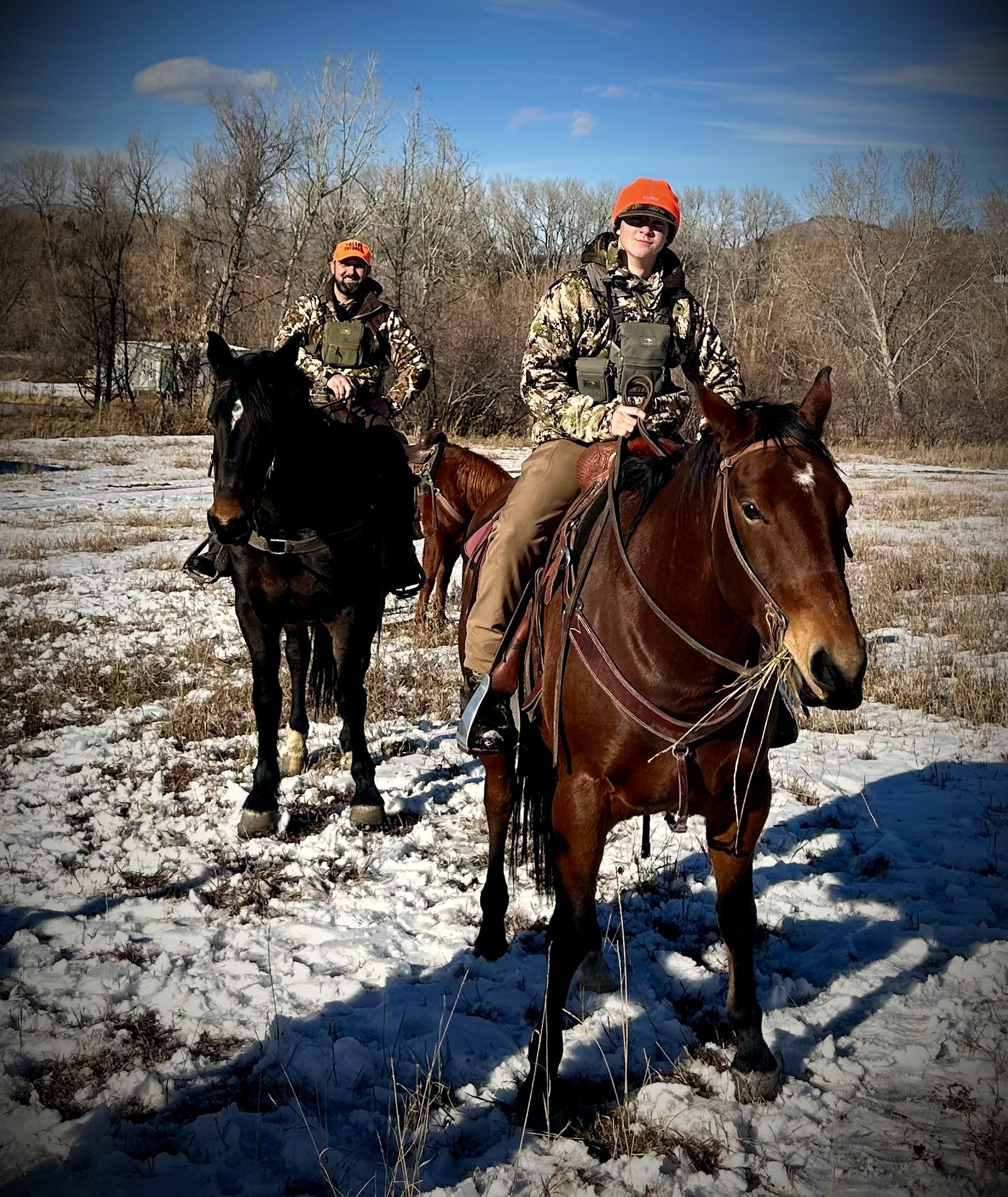 Two riders on horseback crossing a snow-dusted meadow at Heart-J Center