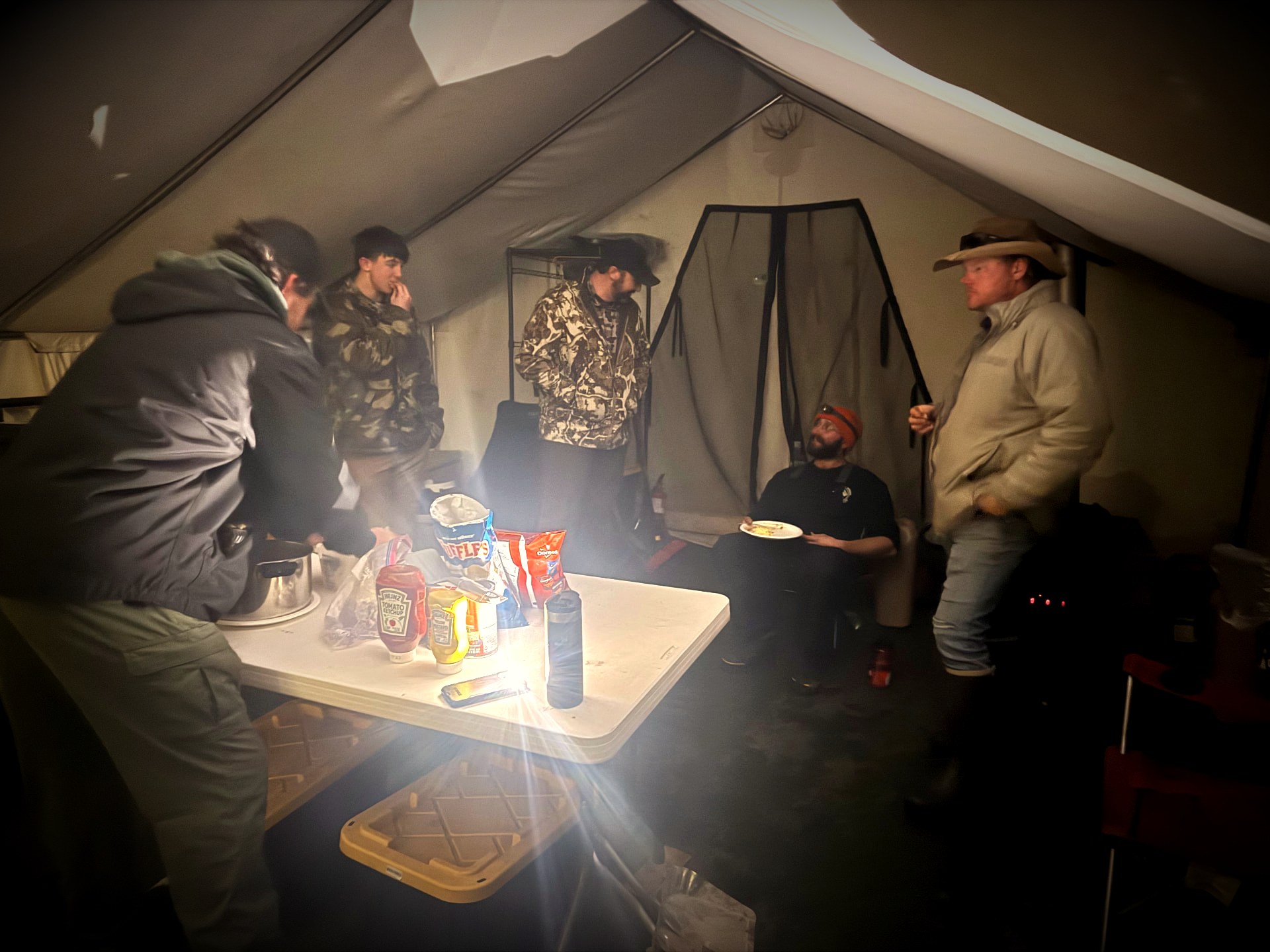 Participants gathered around the table in a lantern-lit wall tent at camp