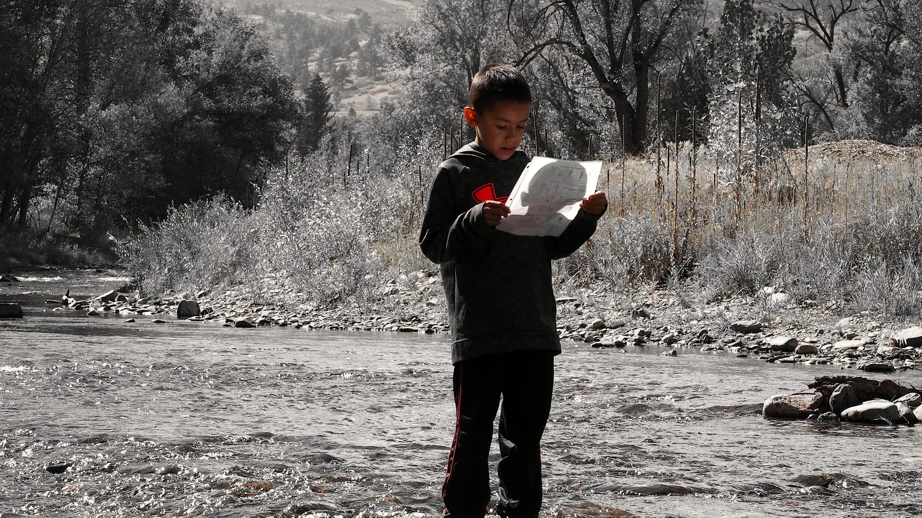 A young person holding a field notebook beside the Big Thompson River
